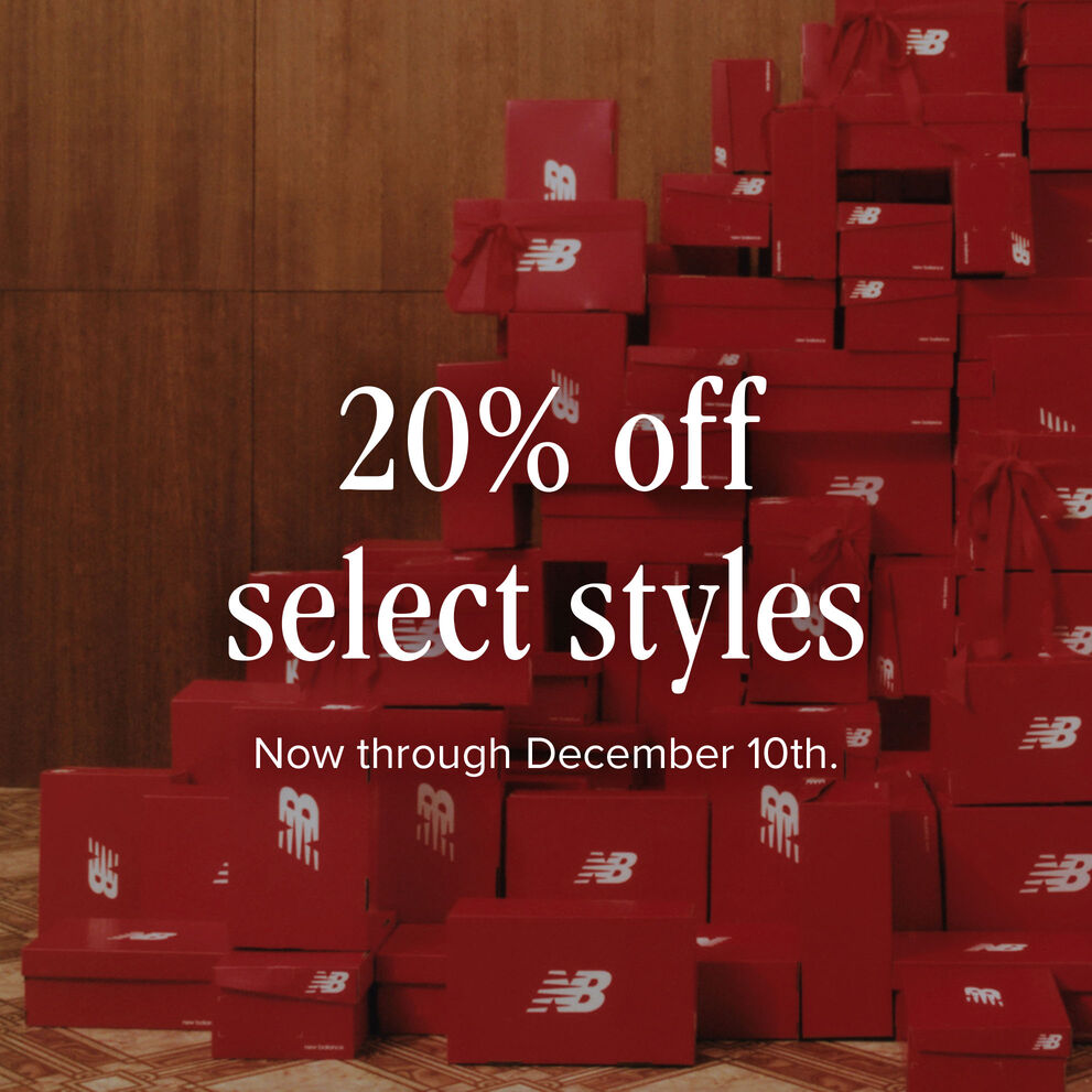 A large stack of red New Balance shoe boxes with red bows attached piled high against a wood panel wall 